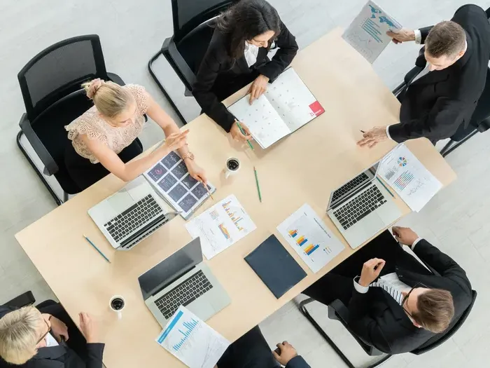 Overhead view of professionals at a meeting table with laptops and charts, planning marketing strategy on townservicehub.com